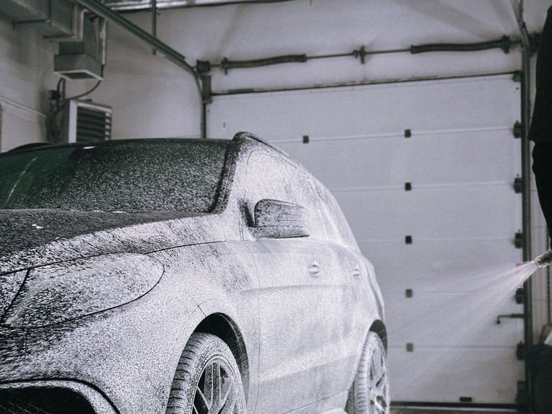 Dark SUV covered in white foam in a car wash bay