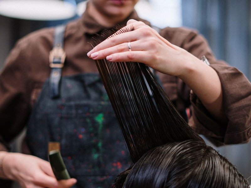 Hair stylist in an apron holding a strand of long dark hair before a cut