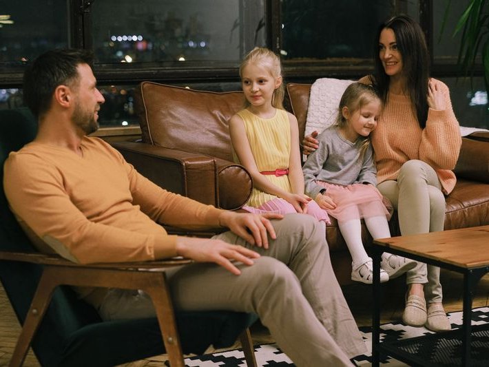 Smiling family of four sitting together on a leather sofa in a cozy living room